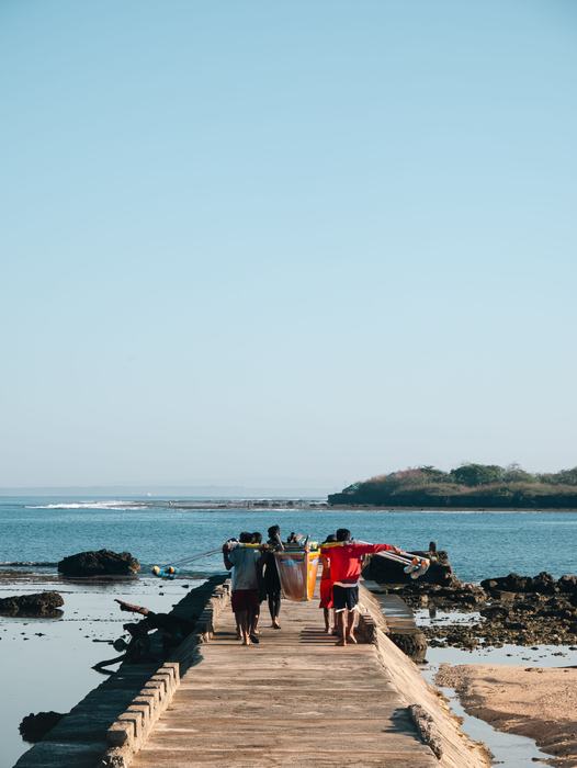 Fishermen carrying an outrigger boat along a stone pier