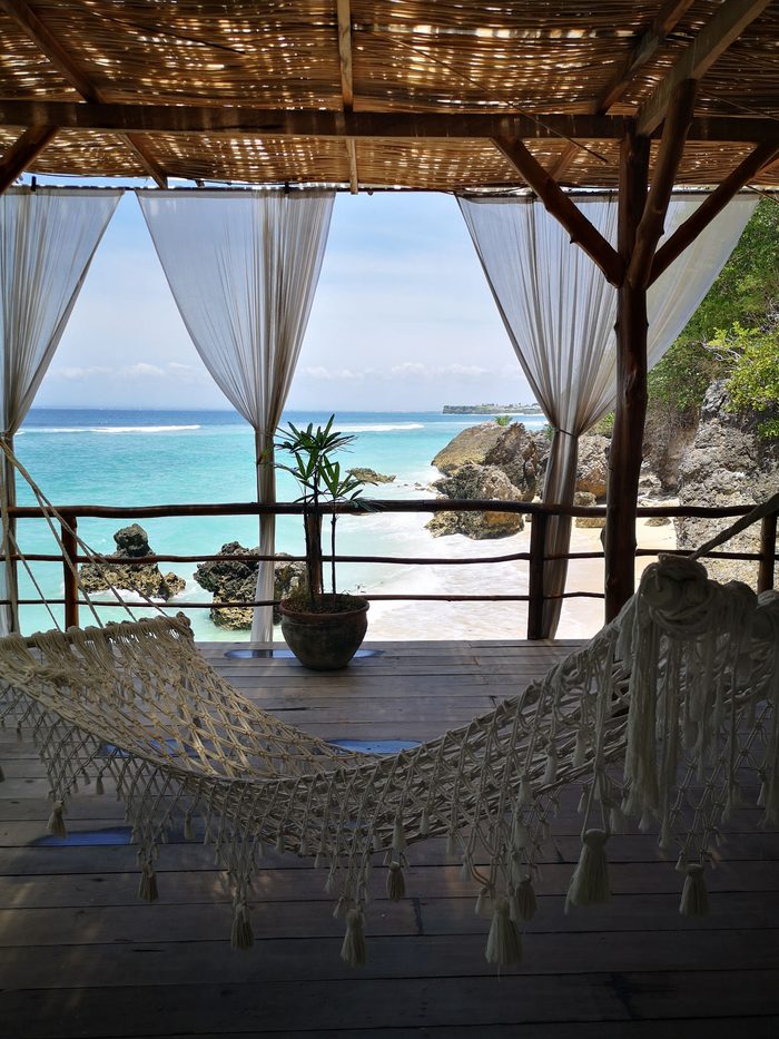 Hammock under a thatched shelter looking out to a turquoise beach